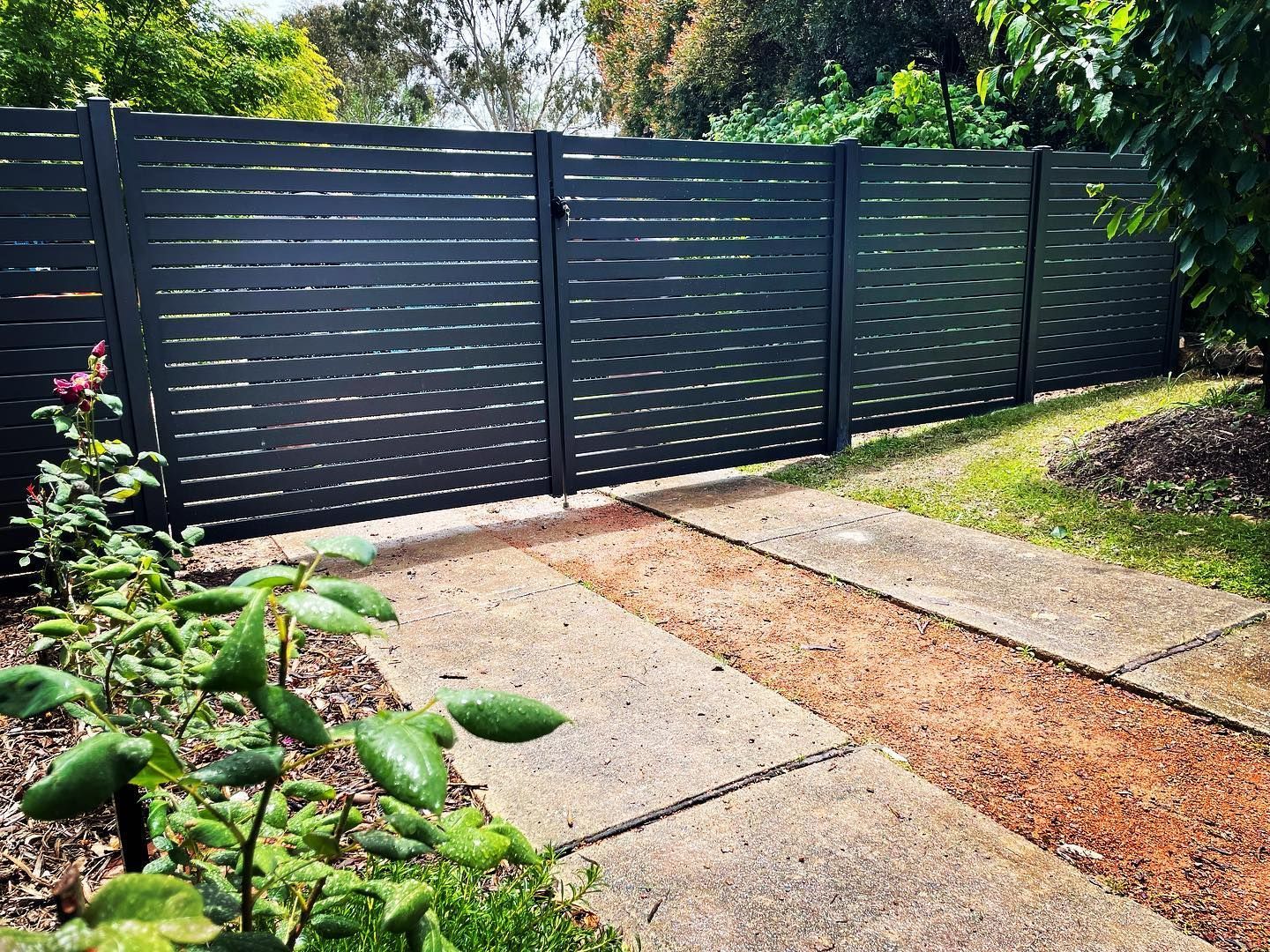 A black fence is surrounding a concrete driveway.