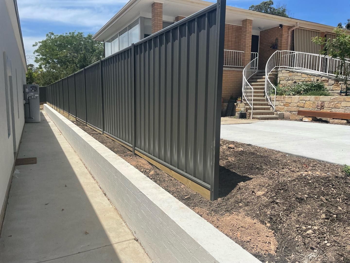 A Colorbond fence along a sidewalk in front of a house.