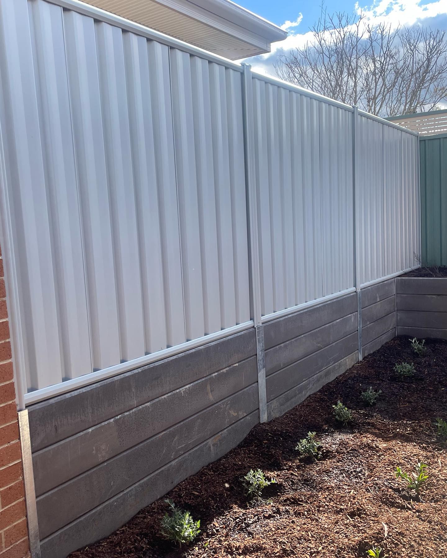 A white fence is sitting next to a brick wall in a backyard.