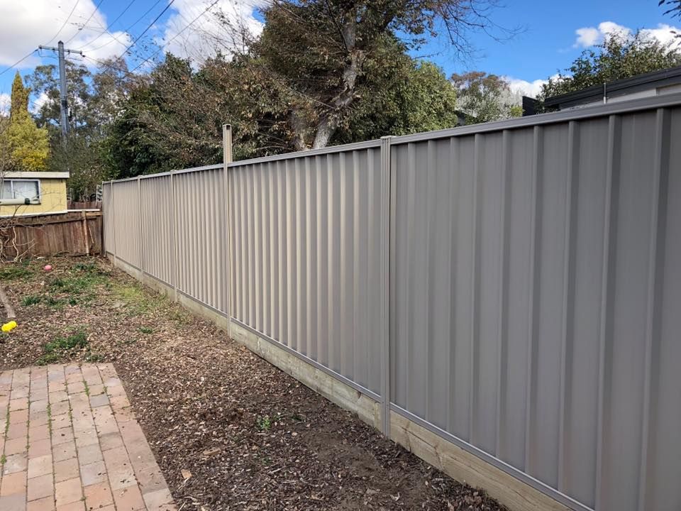 A gray metal fence surrounds a brick walkway in a backyard.