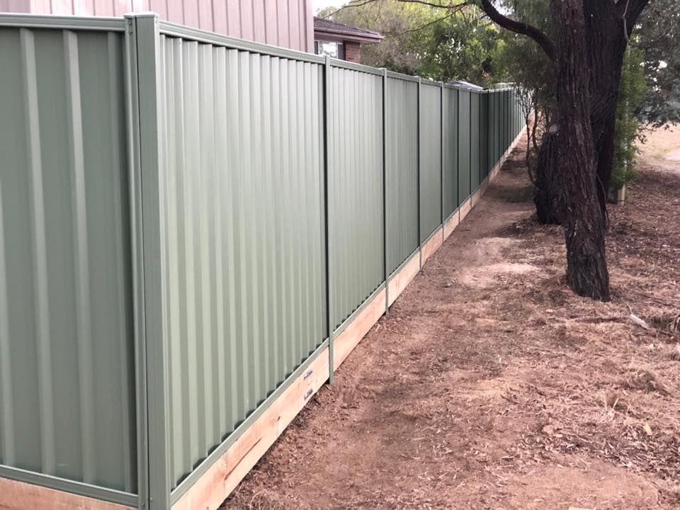 A green fence with a wooden post is surrounded by dirt and trees.