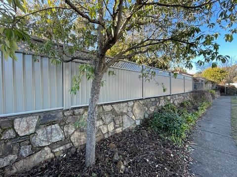 A stone wall with a white fence and a tree in front of it.