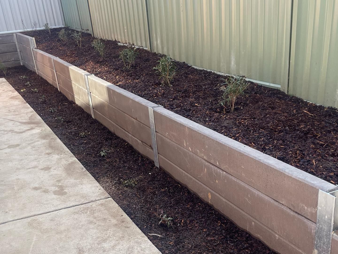 A concrete planter filled with dirt and plants next to a fence.