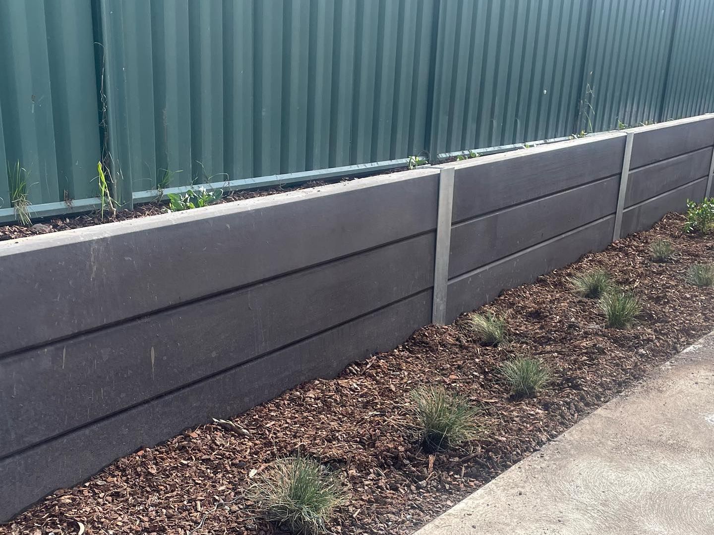 A concrete wall with a green fence in the background