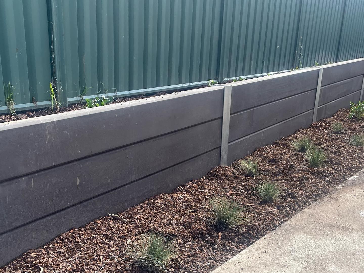 A concrete retaining wall with a green fence in the background