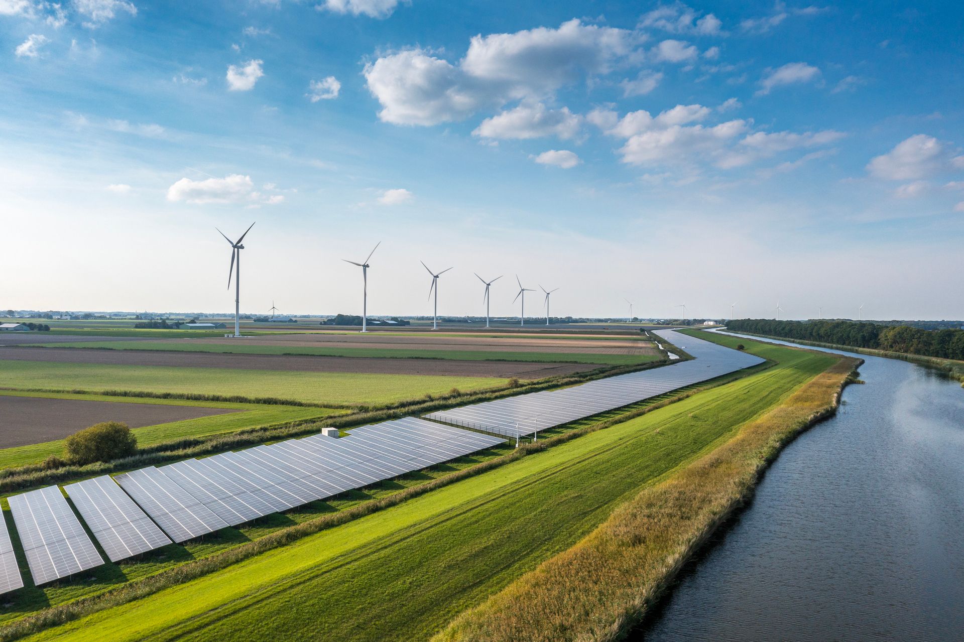 An aerial view of solar panels and wind turbines next to a river.
