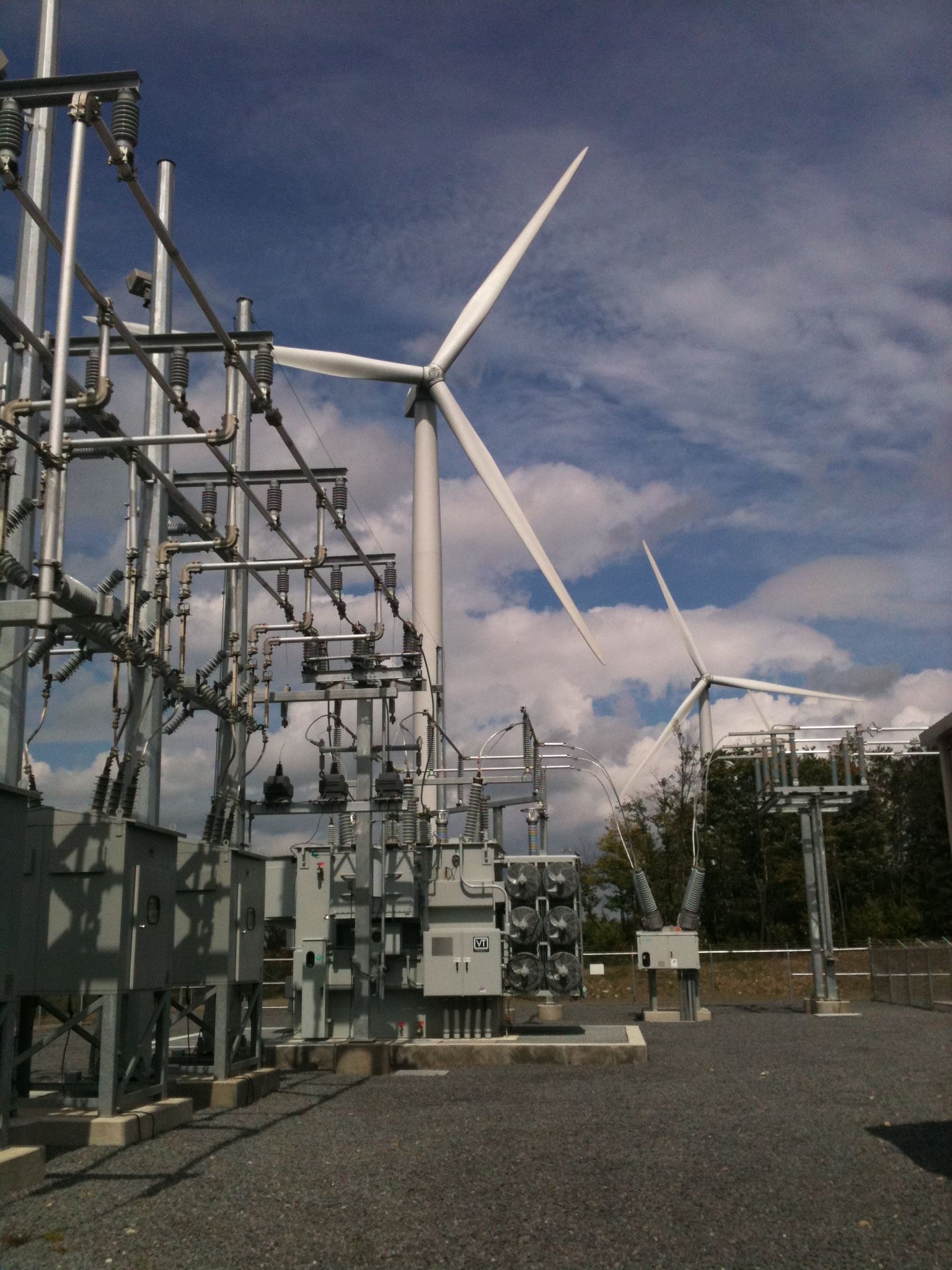 A field of solar panels and wind turbines at sunset.
