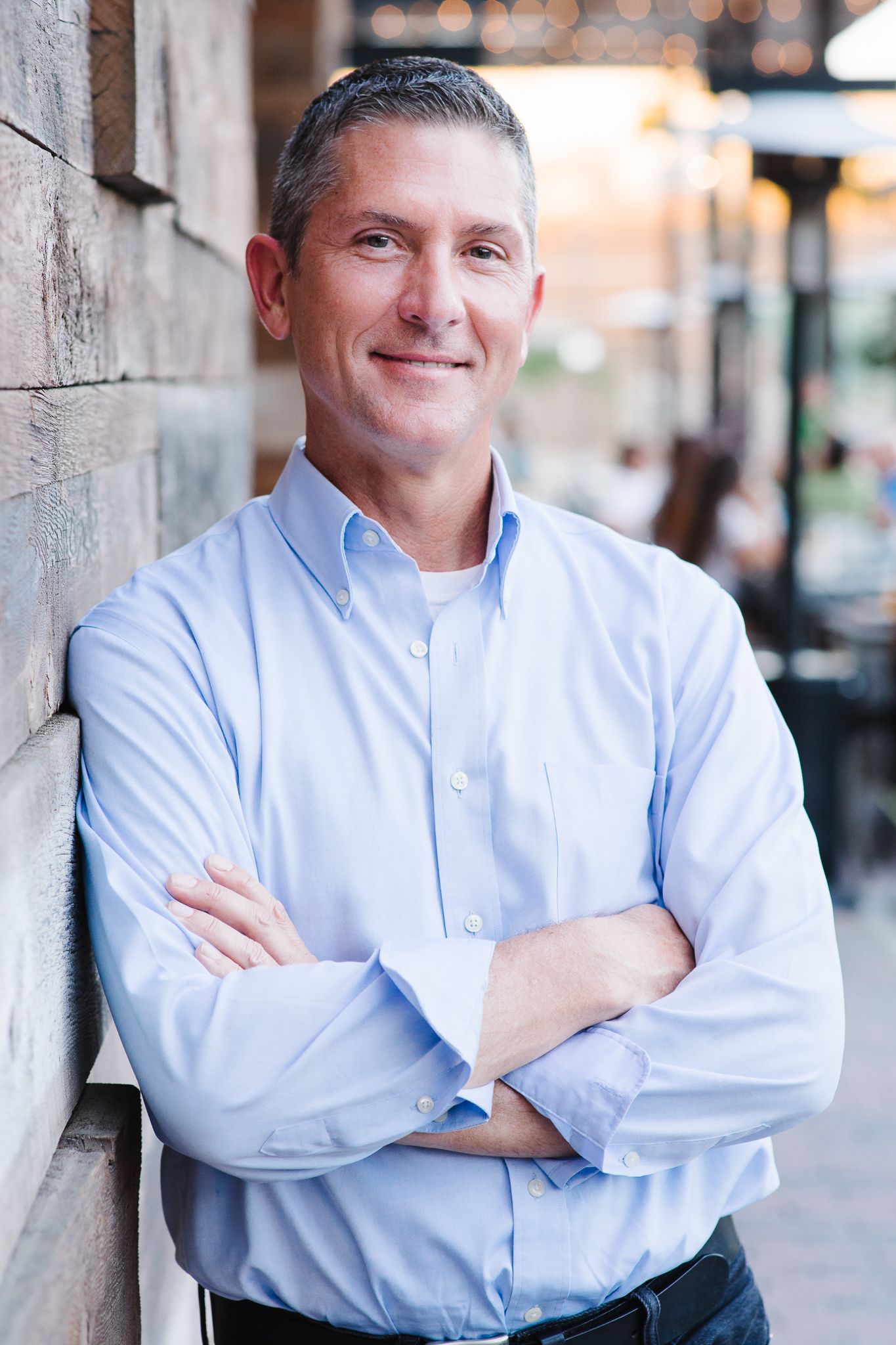 A man in a blue shirt is leaning against a wall with his arms crossed.