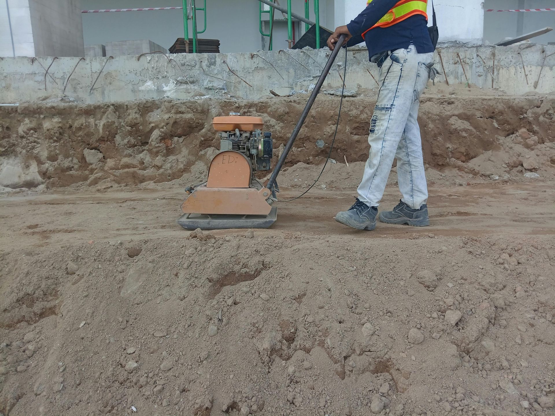 Construction worker using a plate compactor to compact soil on a construction site.