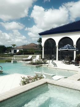 Luxury pool with a mansion, a blue tile roof, and sunny skies.