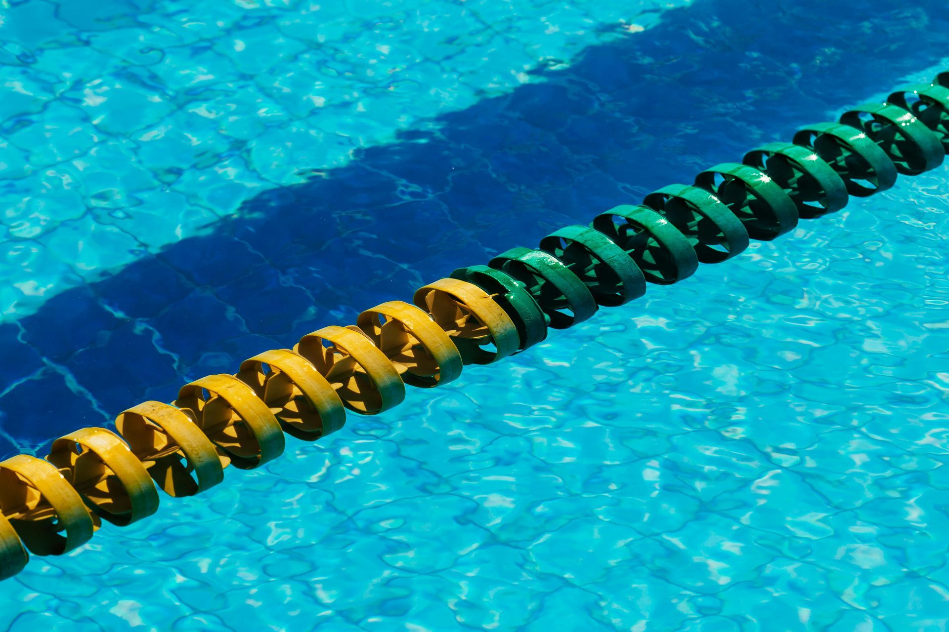 Yellow and green swimming lane markers in a blue pool, creating shadows.