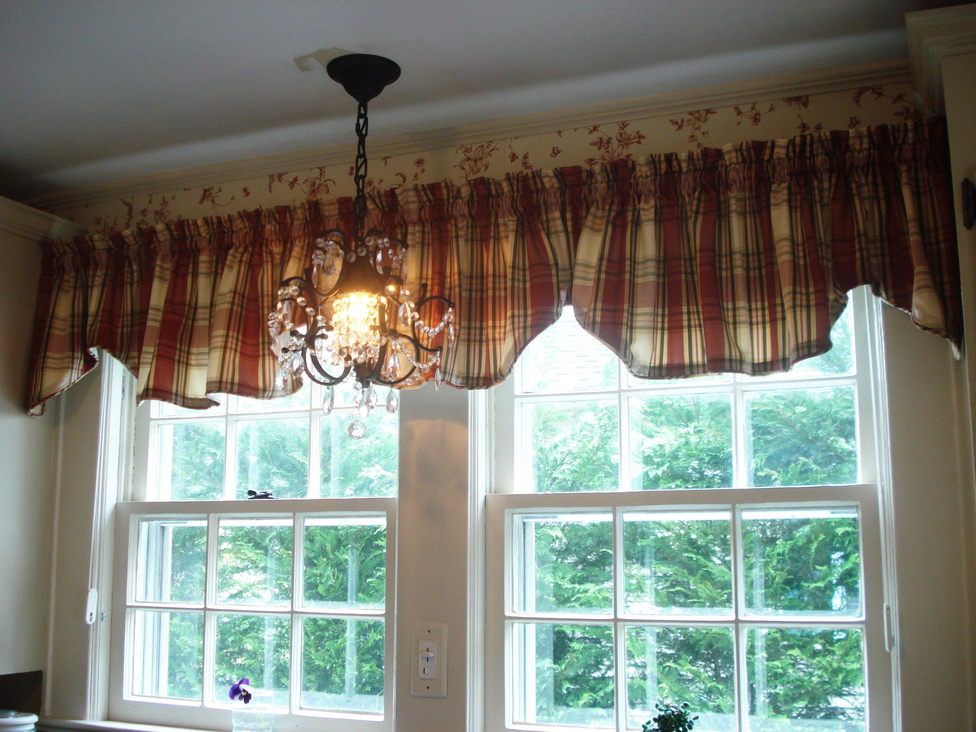 Two windows with a valance and chandelier. The valance is red and beige plaid.