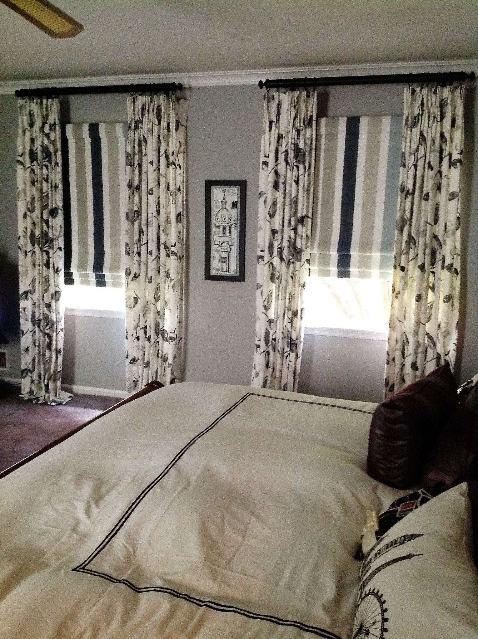 Bedroom with bed, floral curtains, gray wall, and framed artwork.