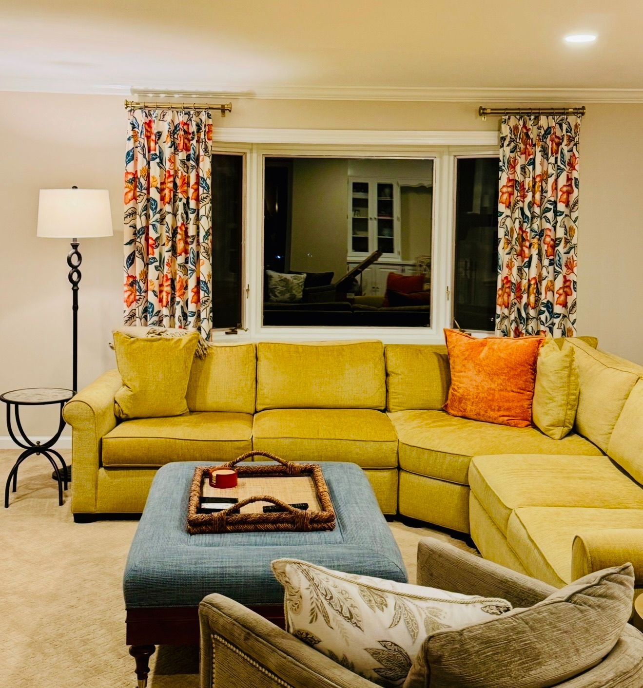 Cozy living room with yellow sectional sofa, patterned curtains, and a window with an outdoor view.