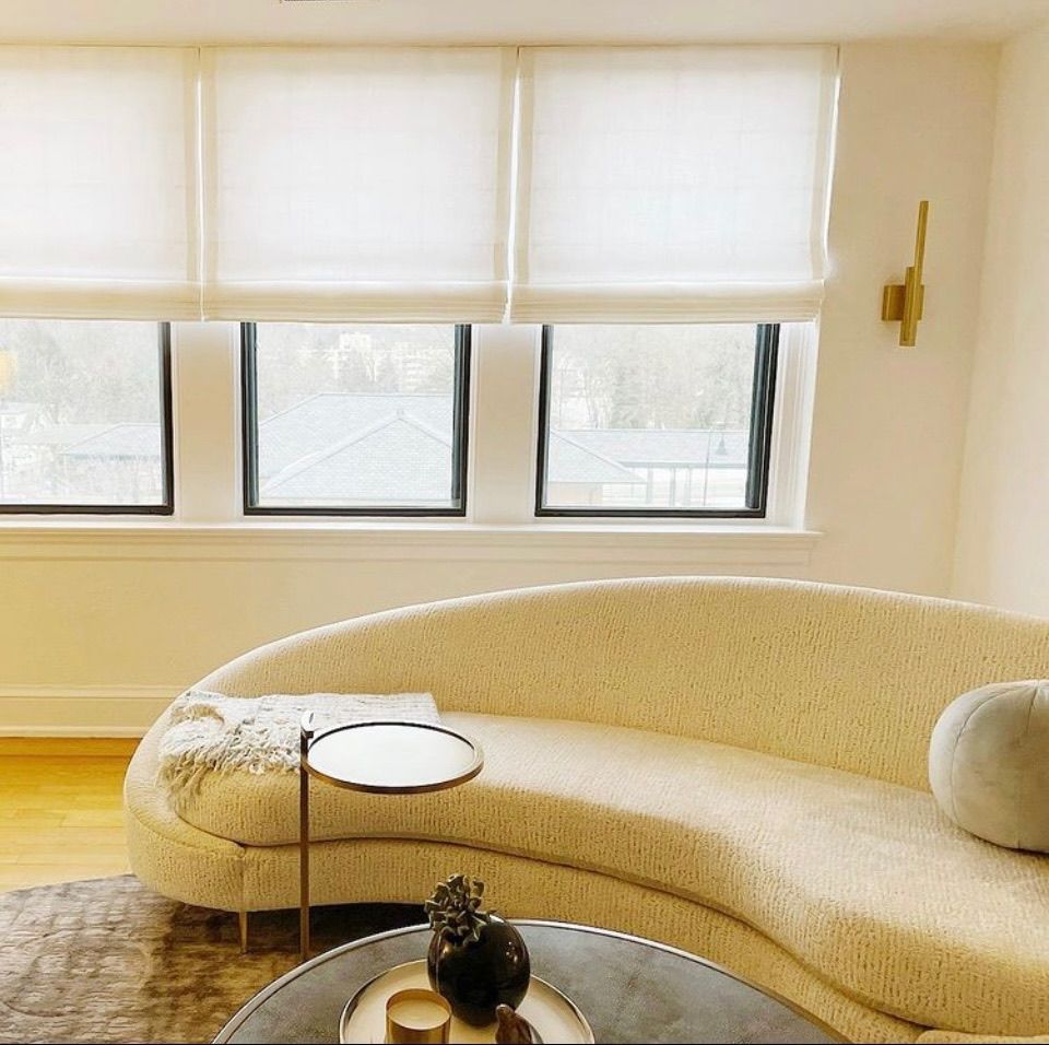 Living room with curved cream couch, round coffee table, and three windows with blinds.