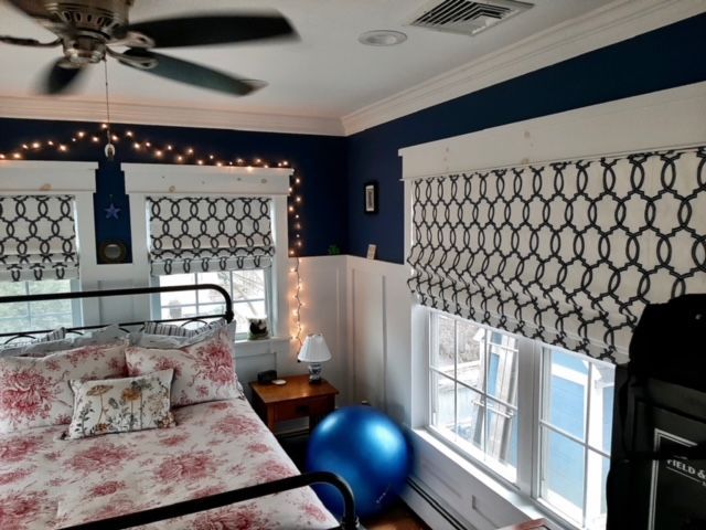 Bedroom with blue and white walls, floral bedding, patterned window shades, and a ceiling fan.