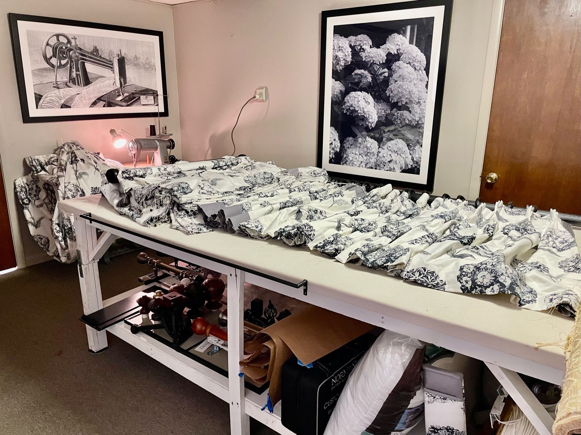 Sewing room with fabric on a large work table, sewing machine, art prints, and storage.