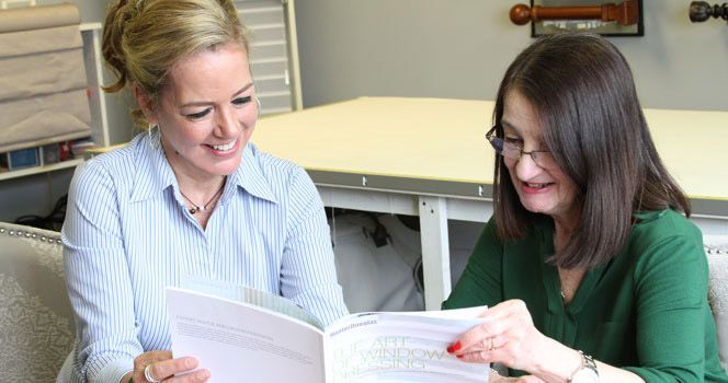 Two women are sitting on a couch looking at a book.