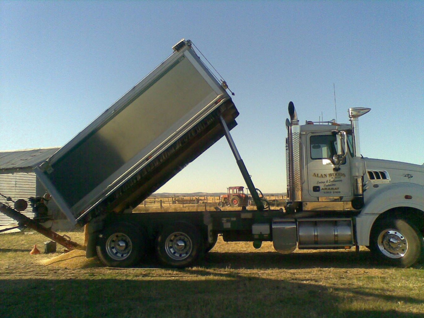 A dump truck is parked in a field and the side of the truck has the word mack on it