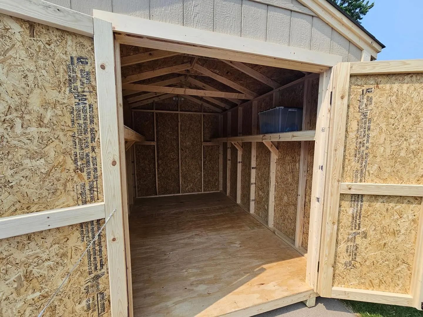 Open wooden shed with a shelf, viewed from the doorway. Walls are made of OSB.