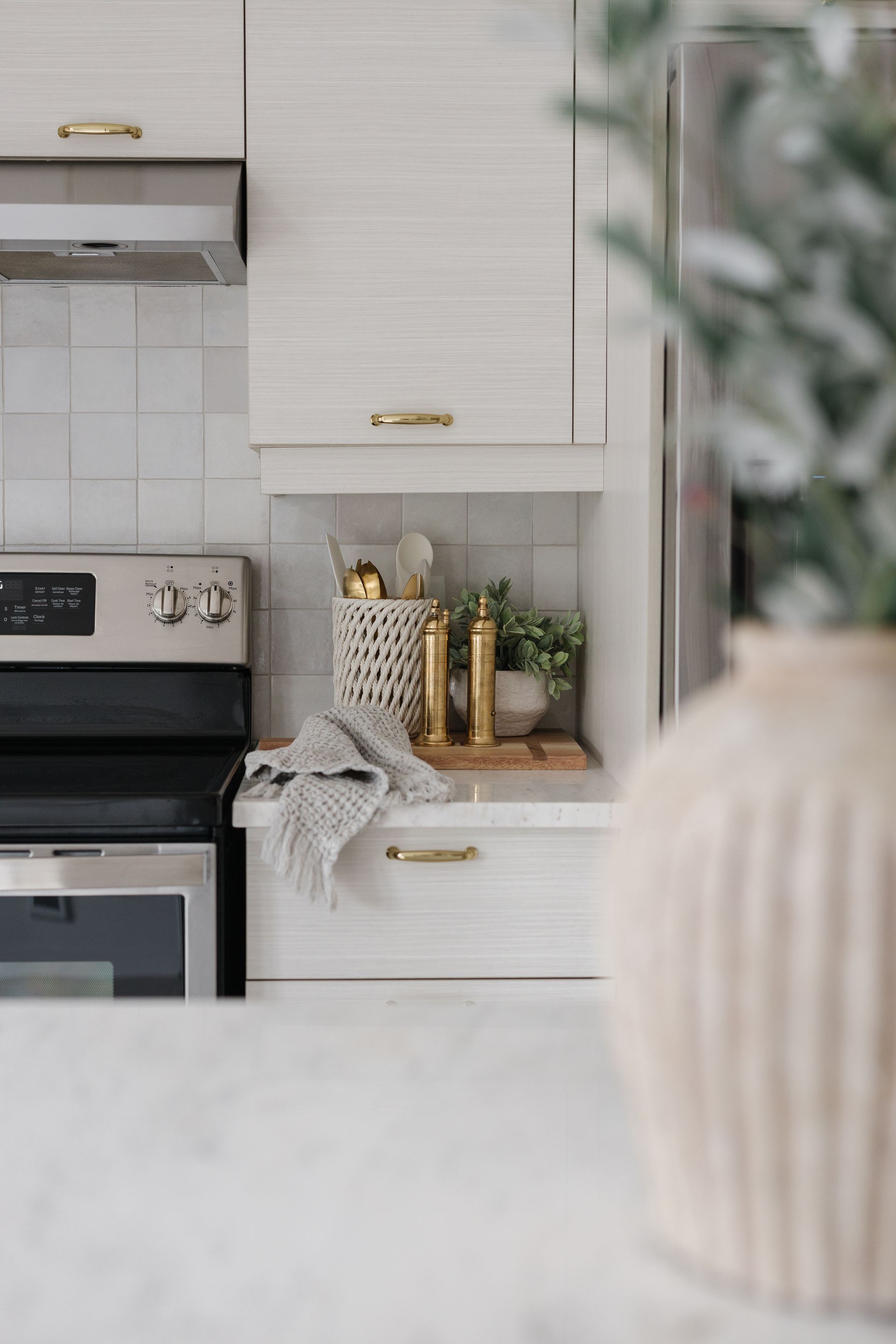 Kitchen interior with light wood cabinets, stainless steel appliances, gold hardware, and decorative items.