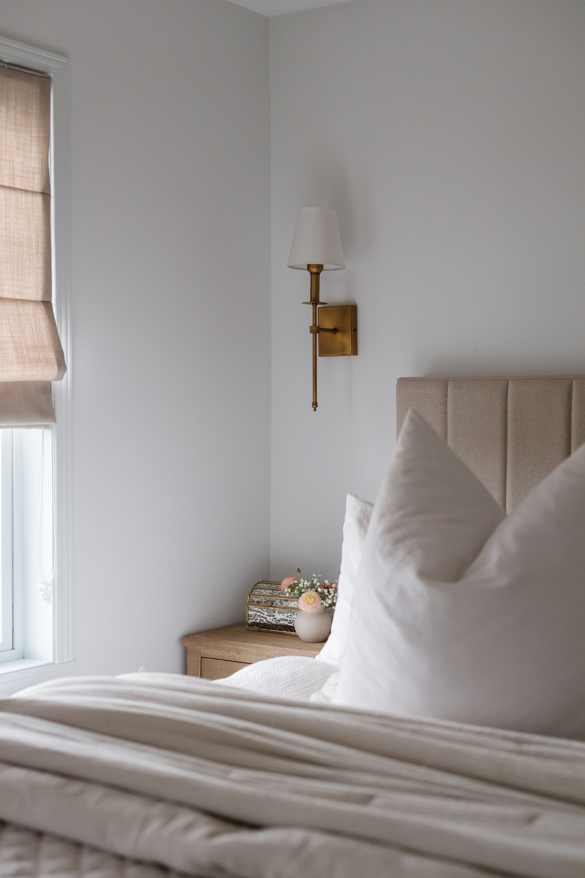 Bedroom corner with a bed, nightstand, sconce, and window with a shade.