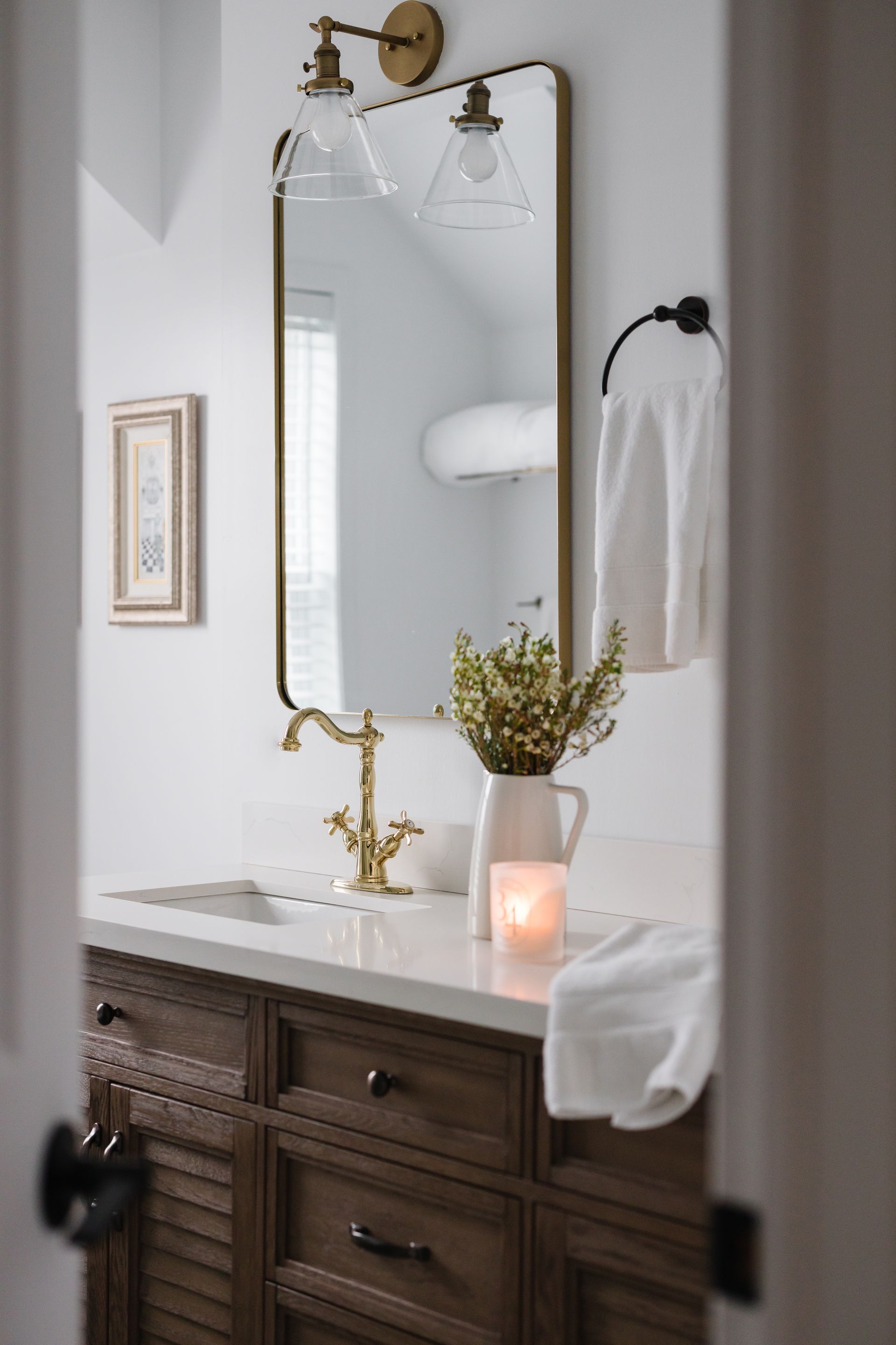 Bathroom with gold fixtures, white walls, wood vanity, mirror, and decorative vase.