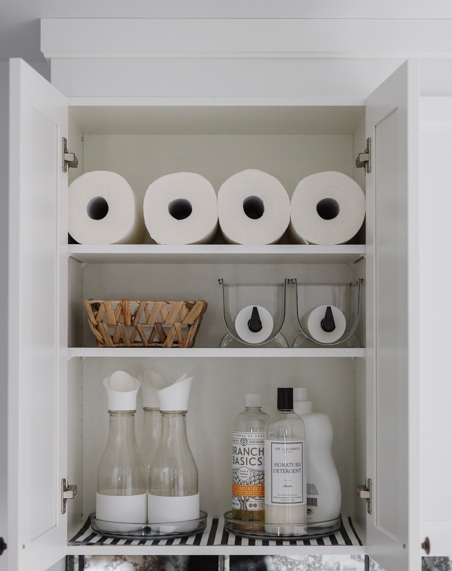 Armoire blanche contenant des rouleaux d'essuie-tout, des récipients et des produits de nettoyage.