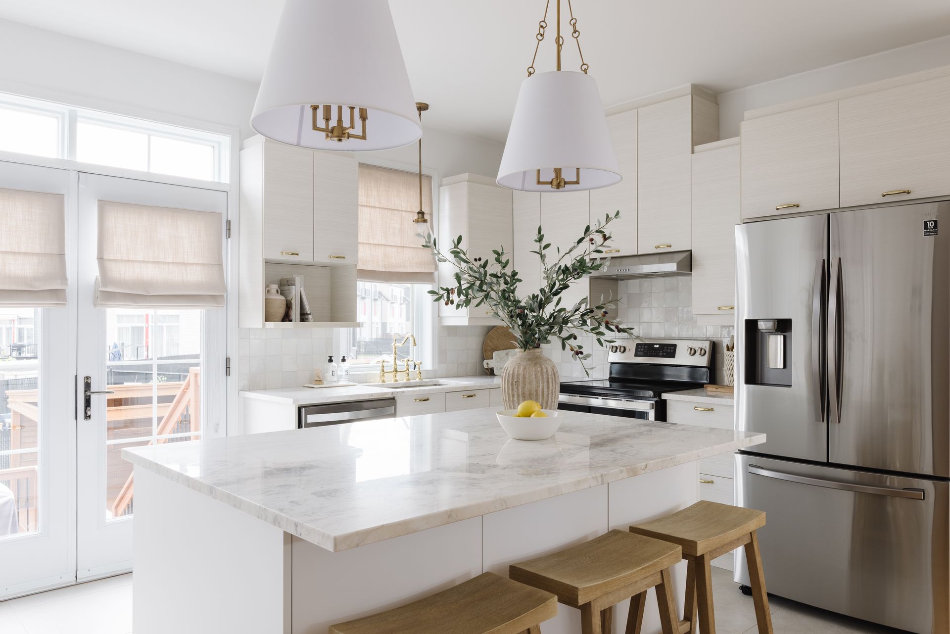 White kitchen with a marble island, stainless steel appliances, and two hanging lamps.