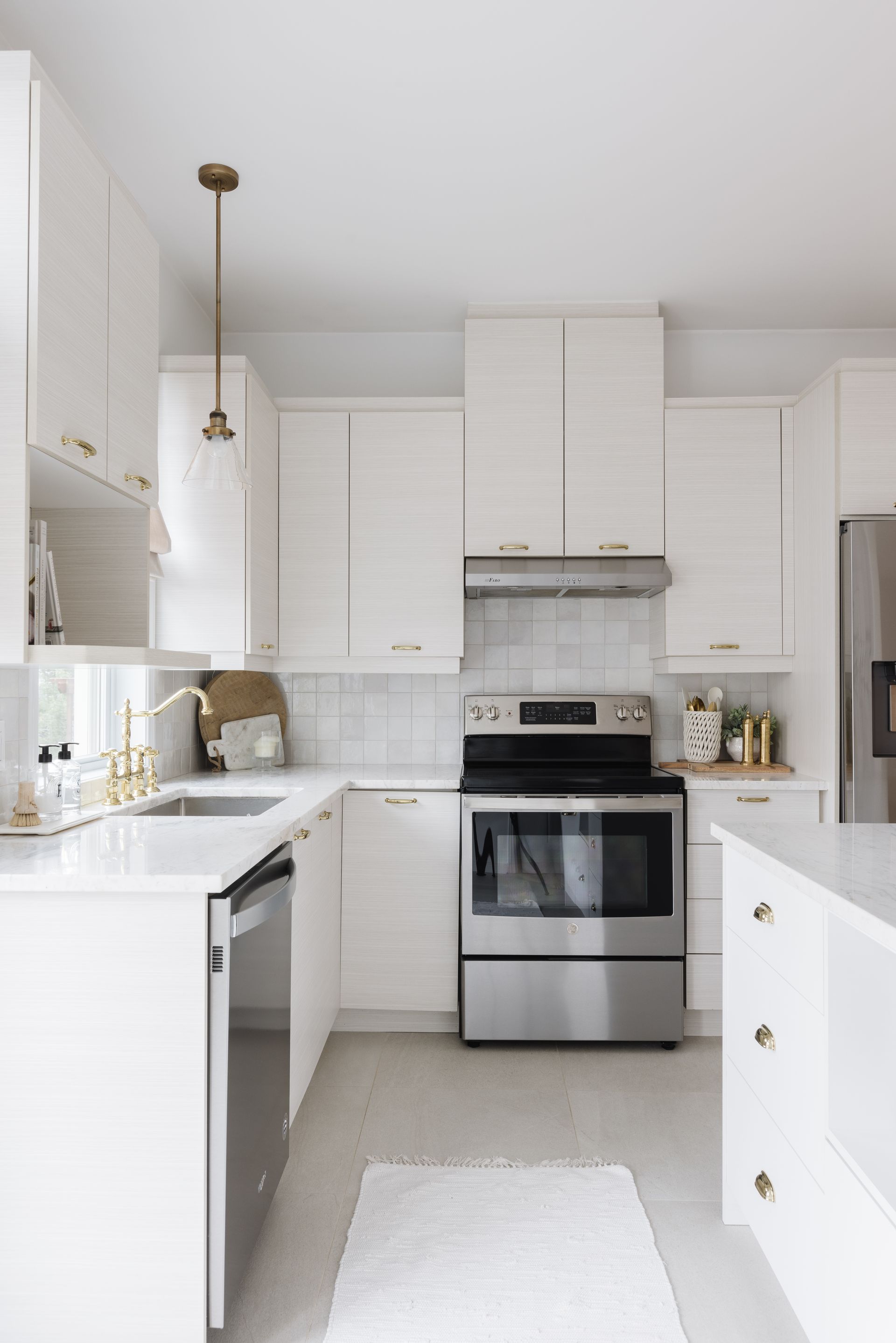 White modern kitchen with stainless steel appliances, white cabinets, and gold hardware.