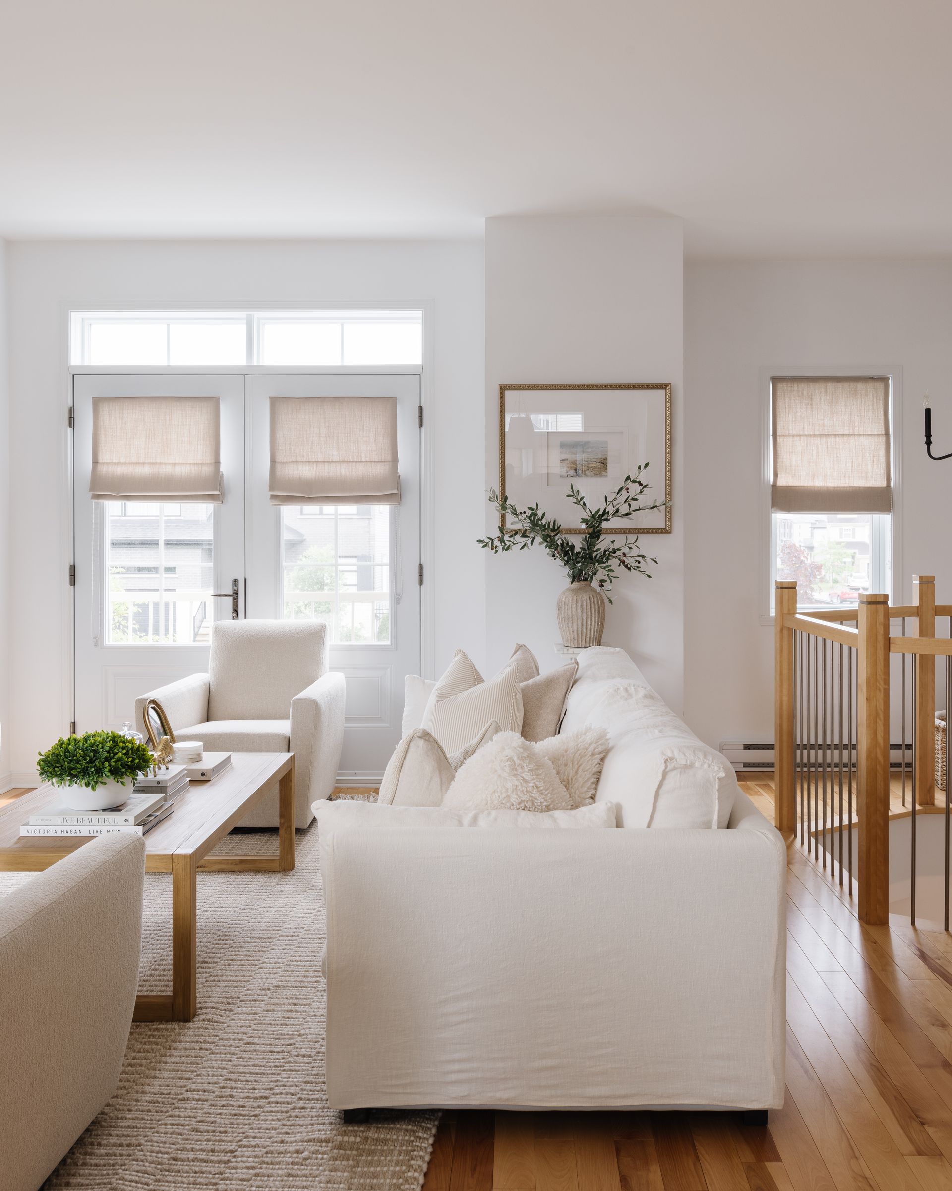 Bright living room with white furniture, wooden floors, and woven shades.
