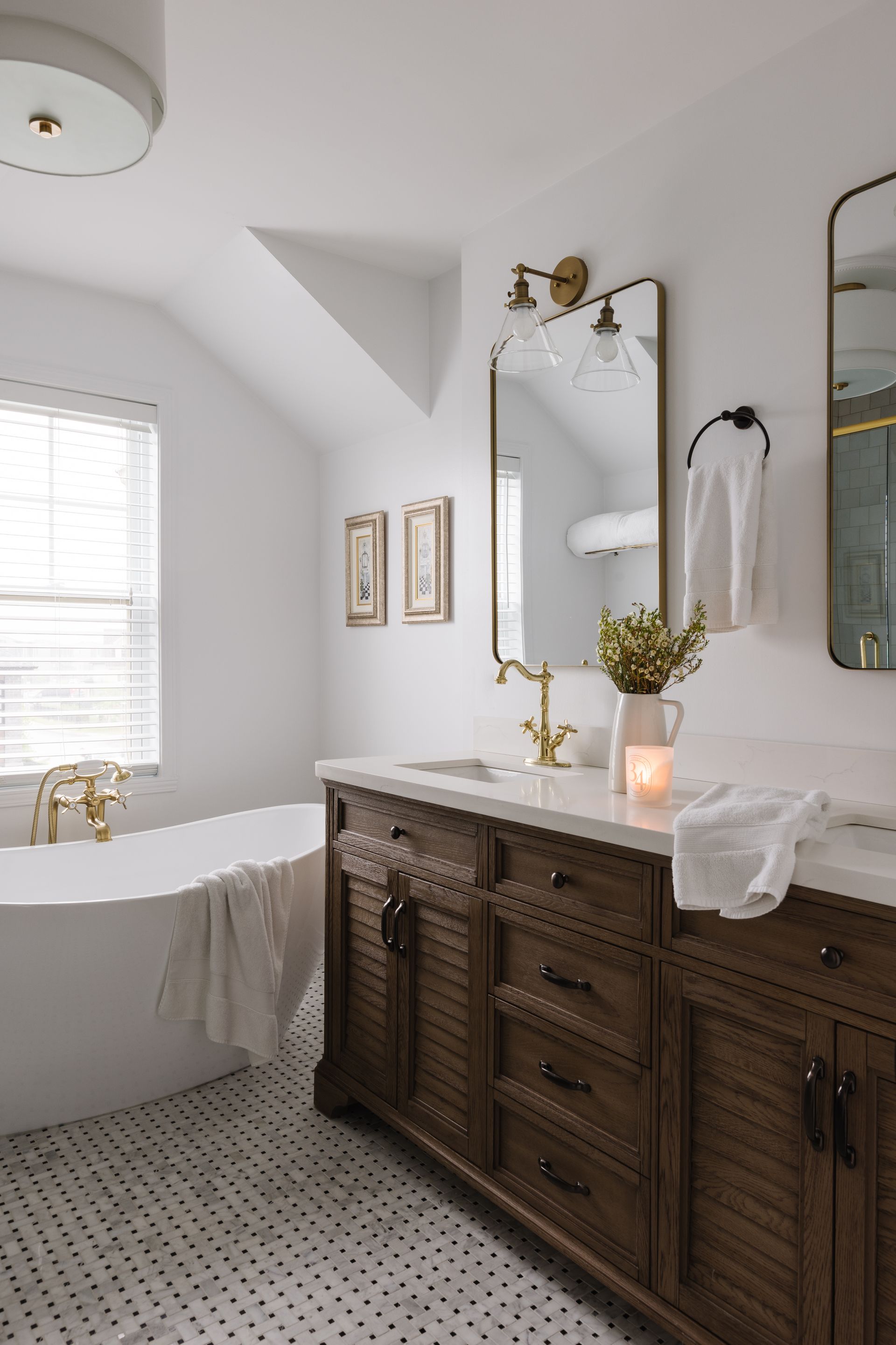 Bathroom with wood vanity, soaking tub, and gold accents. White walls, marble floor.