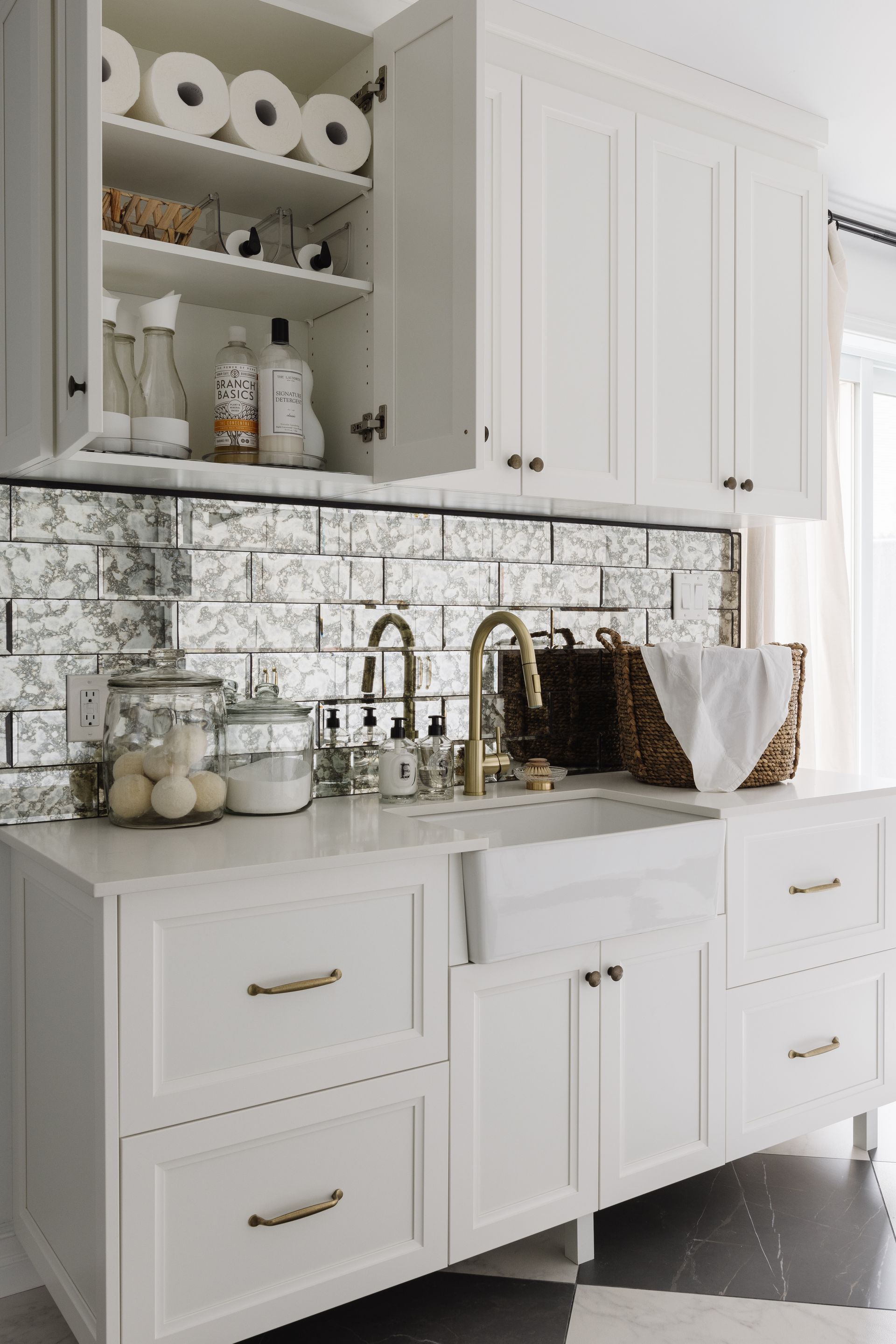 White laundry room with mirrored backsplash, gold fixtures, and farmhouse sink.