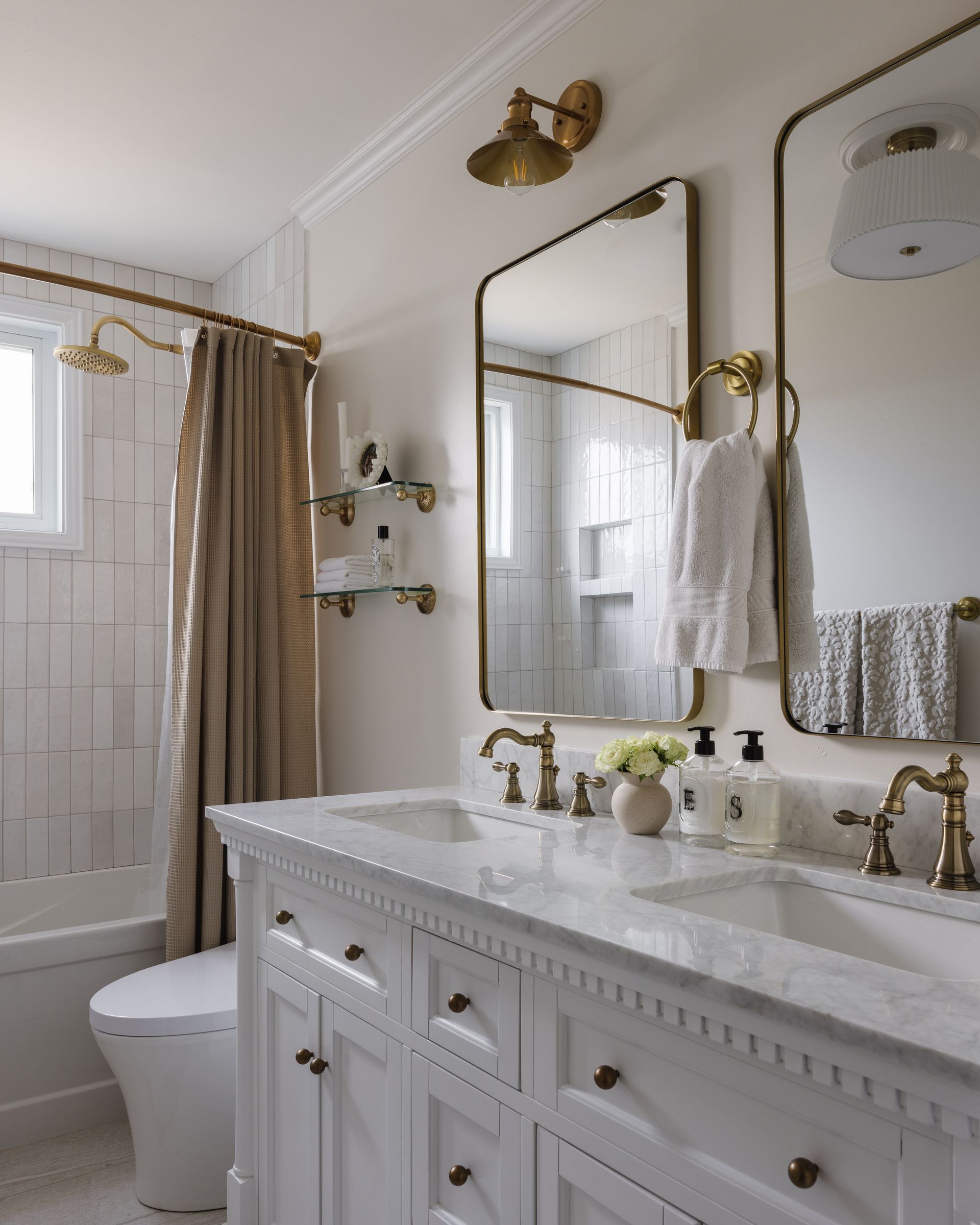 Elegant white bathroom with marble vanity, brass fixtures, and a shower with a tan curtain.