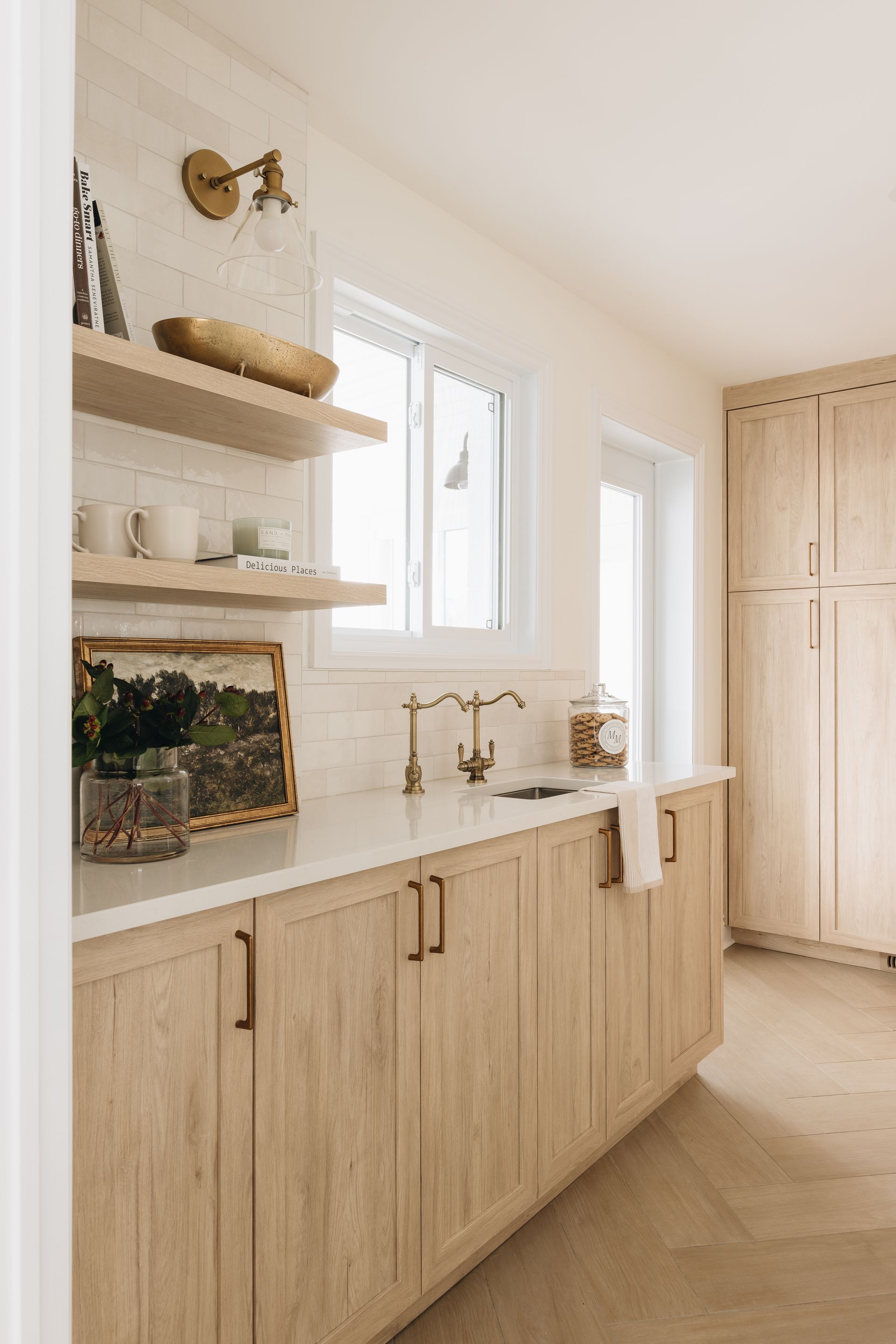 Light-toned kitchen with wooden cabinets, open shelves, and a window. Includes a sink, countertop, and a storage pantry.
