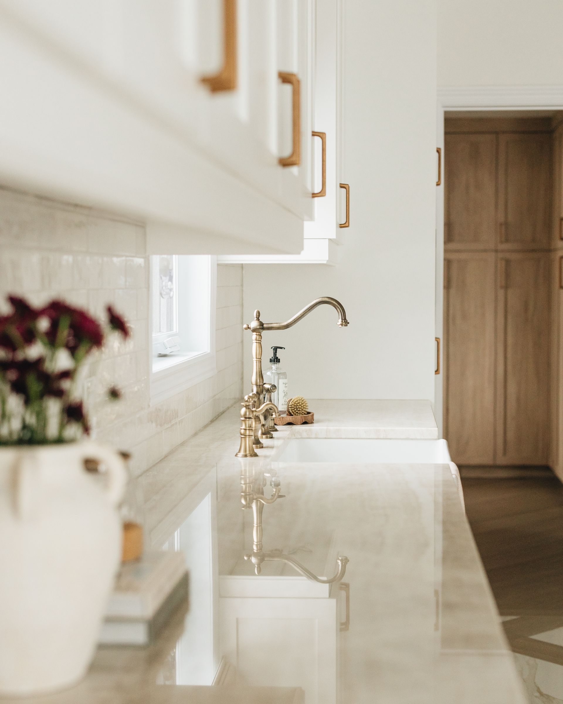 Kitchen with white cabinets, gold hardware, and a gold faucet. White countertops and a vase of flowers.