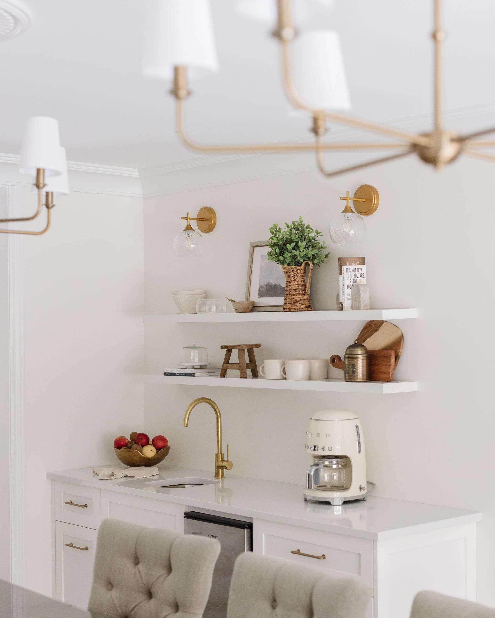 Bright kitchen counter with gold faucet, coffee maker, and shelves holding decor.