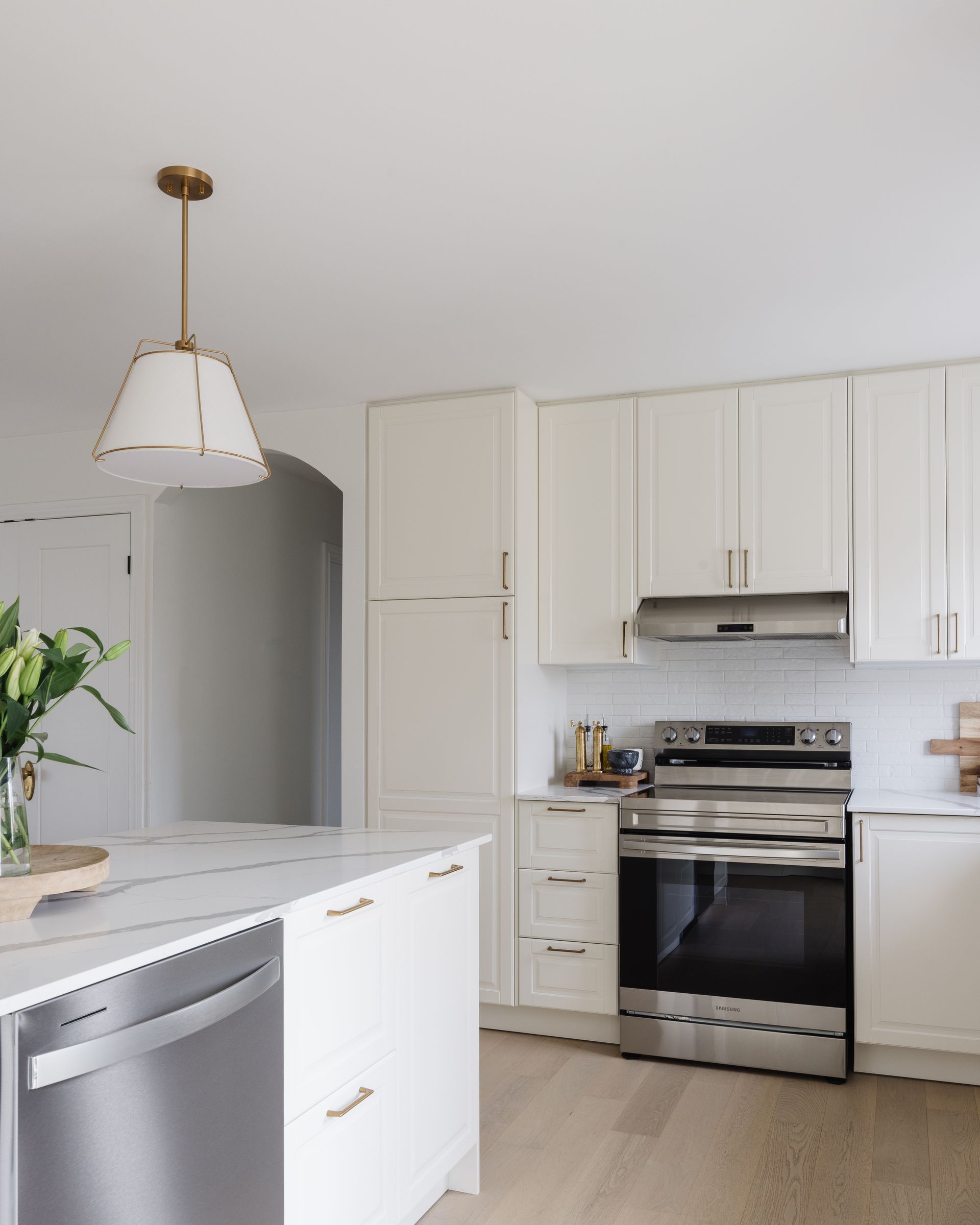 White kitchen with marble countertop, stainless steel appliances, and gold pendant light.
