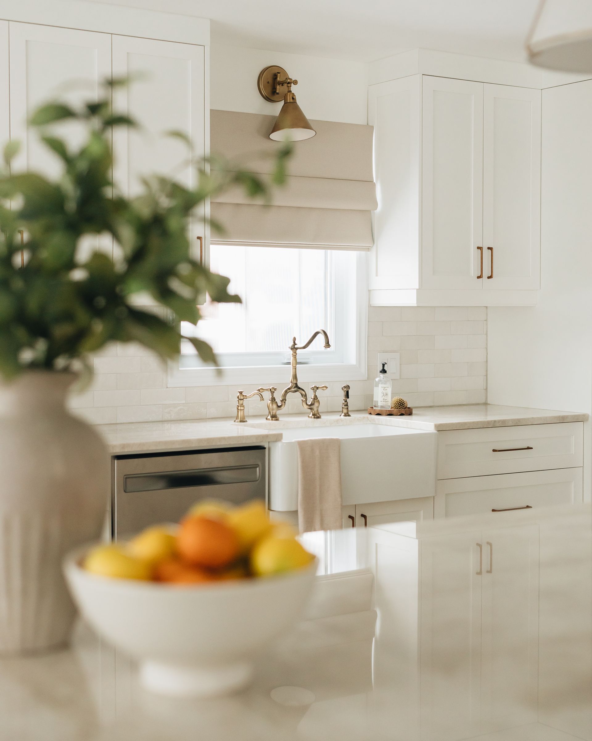Bright white kitchen with brass accents; fruit bowl in foreground.