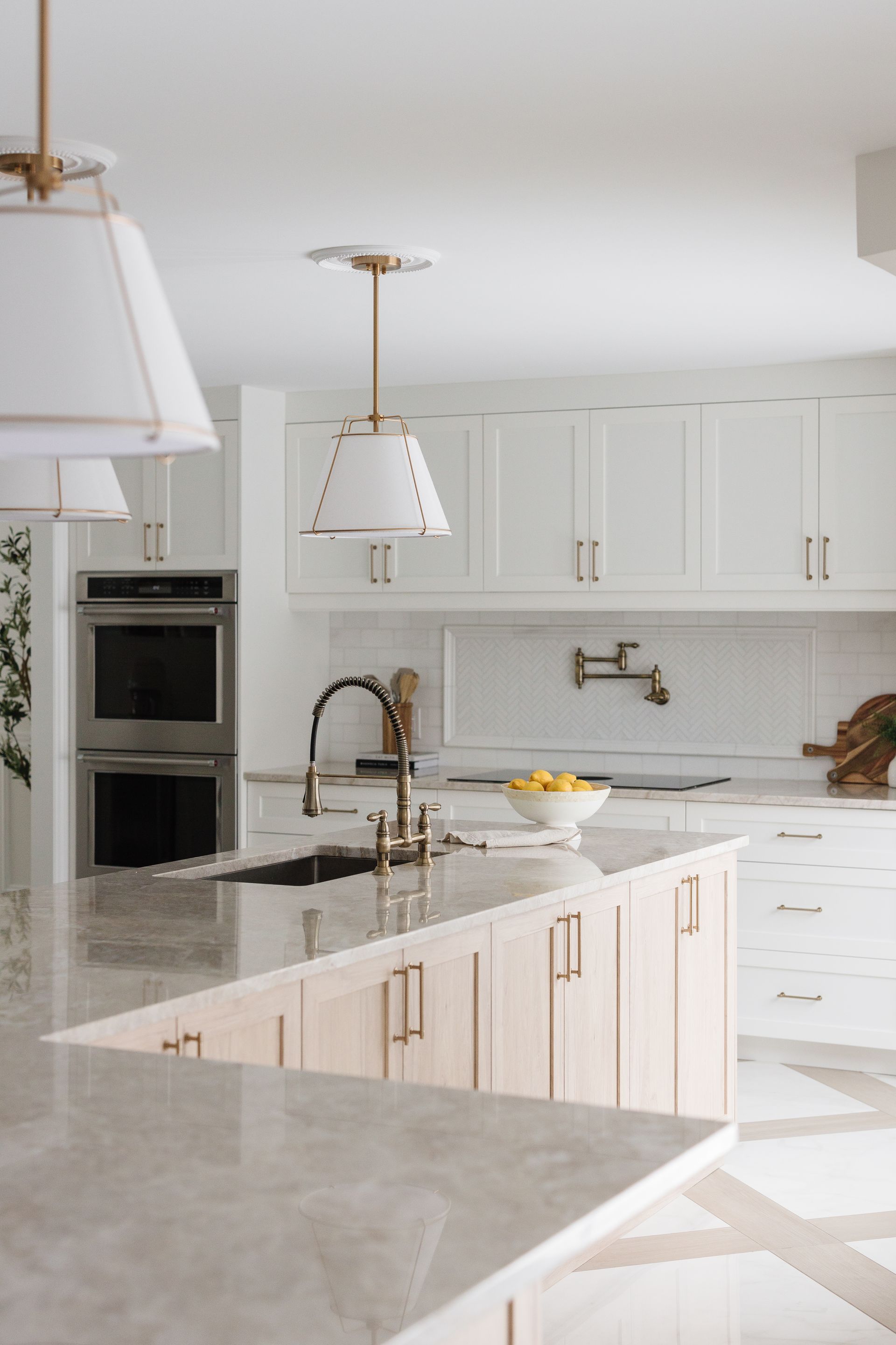 Bright white kitchen with a light wood island, gold fixtures, and overhead pendant lights.