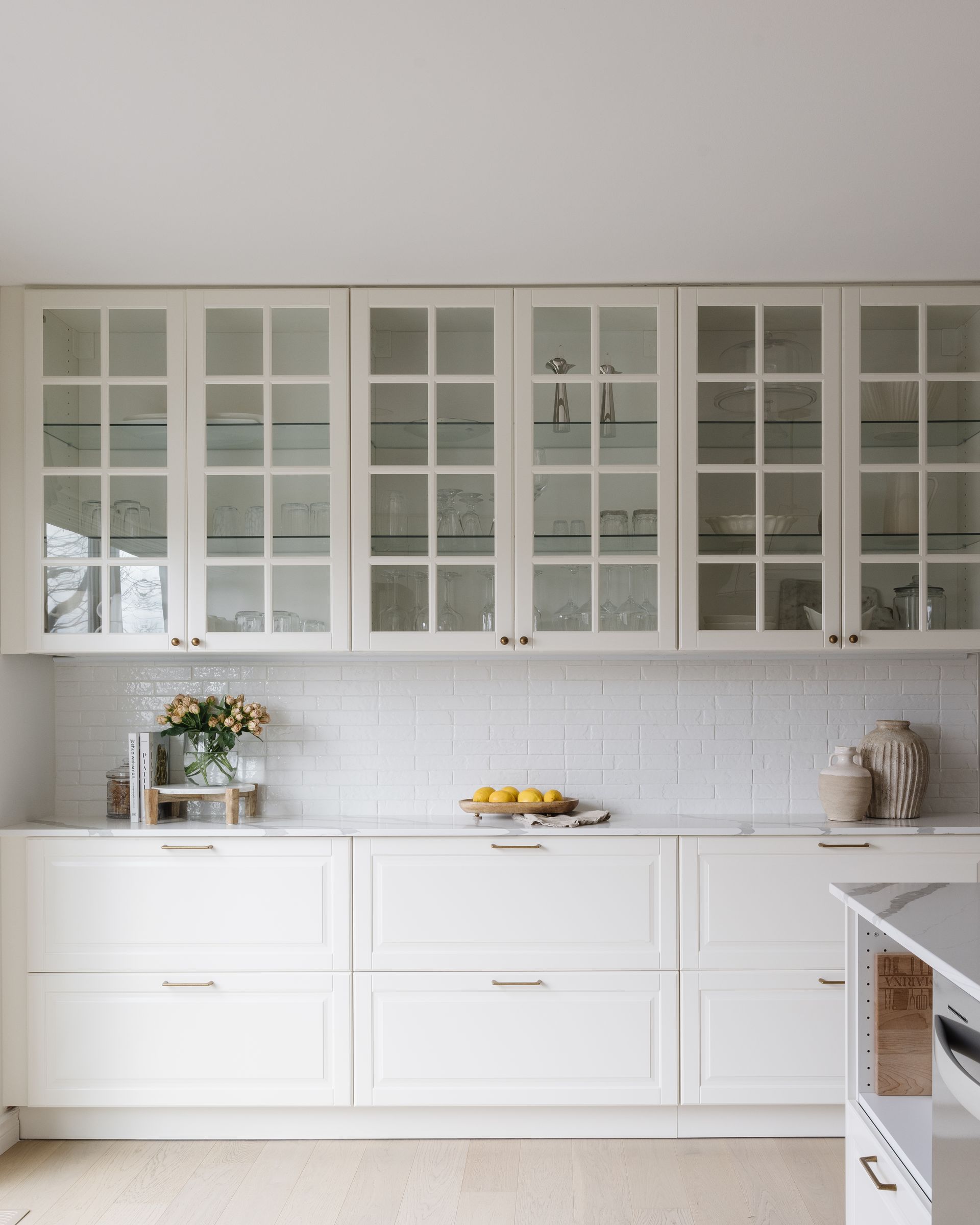 White kitchen cabinets with glass-front uppers and white tile backsplash.
