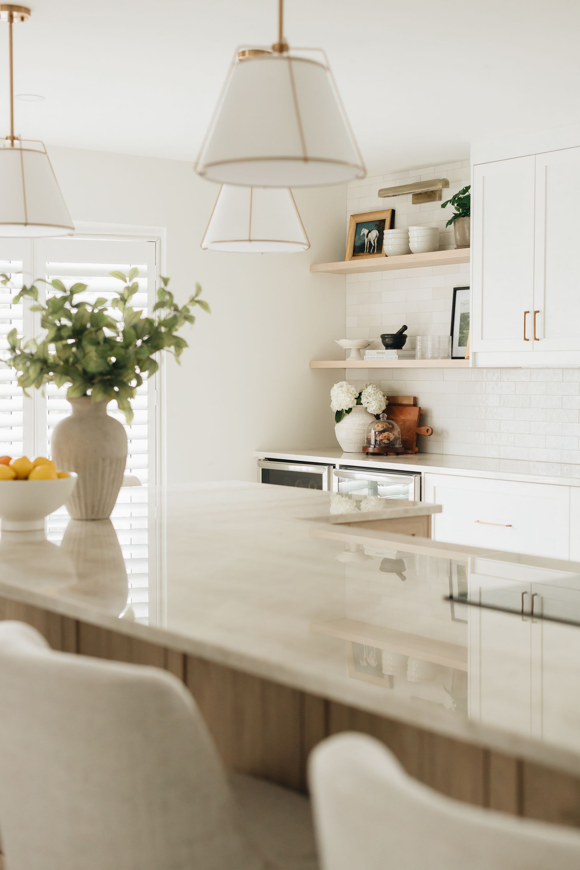 Elegant white kitchen with marble countertop, open shelves, and pendant lights.