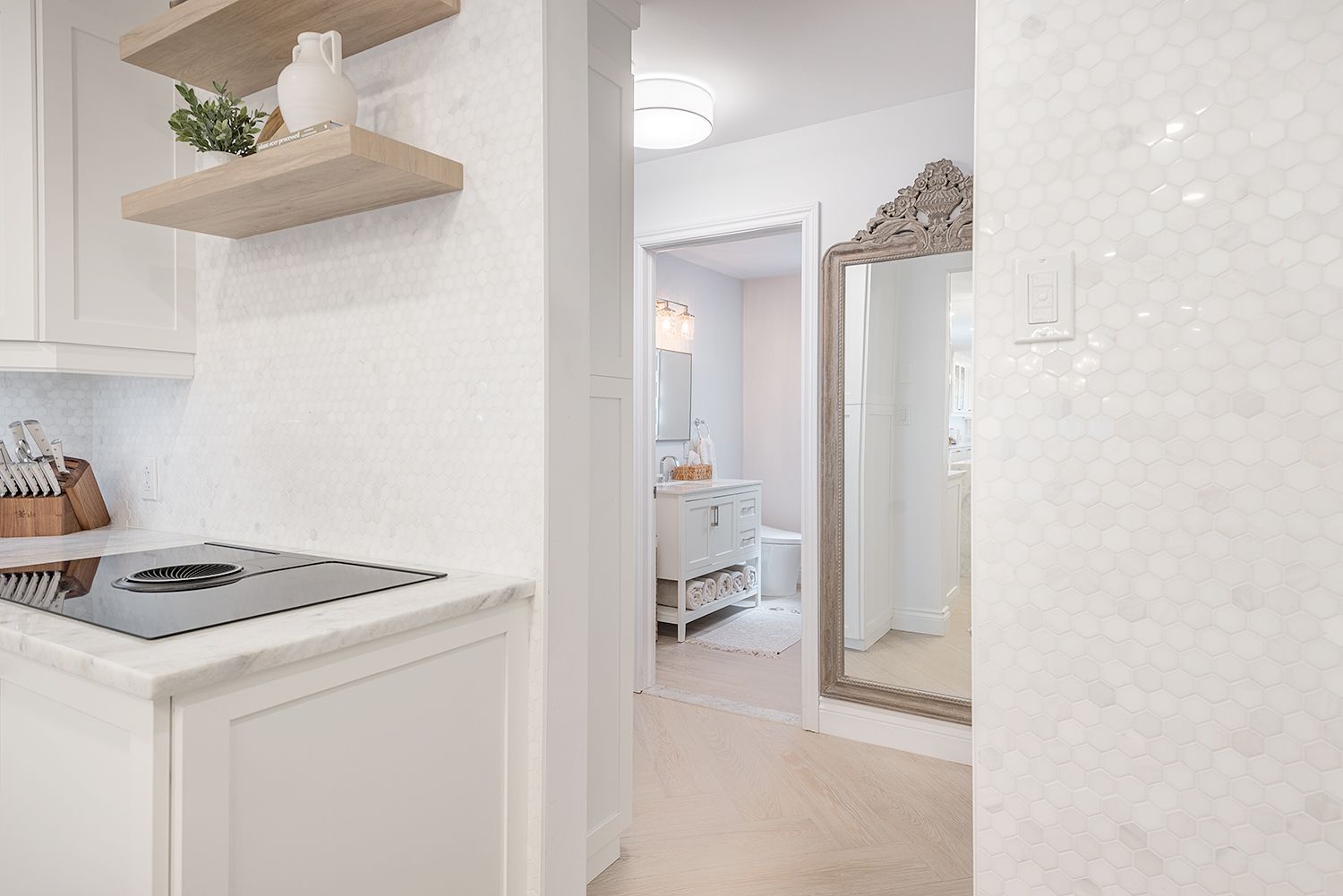 Kitchen and hallway with white walls, cabinets, and a large mirror.