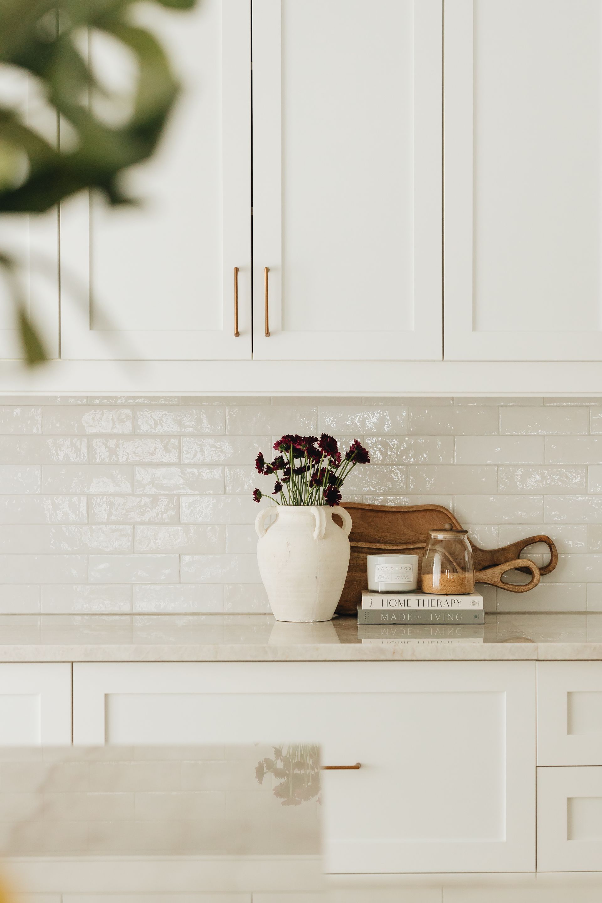 White kitchen with floral arrangement, cutting board, and candles on countertop.