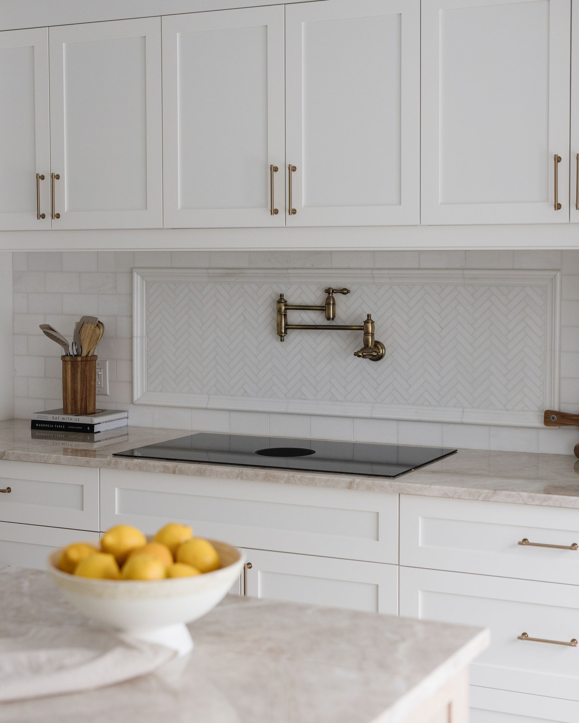 White kitchen with cabinets, stove, and a bowl of lemons. Gold faucet and hardware.