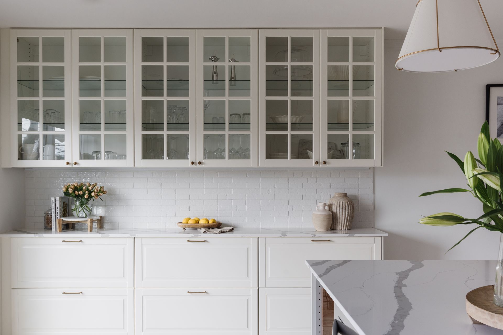 White kitchen cabinets with glass-front uppers, white subway tile backsplash, and gold hardware.