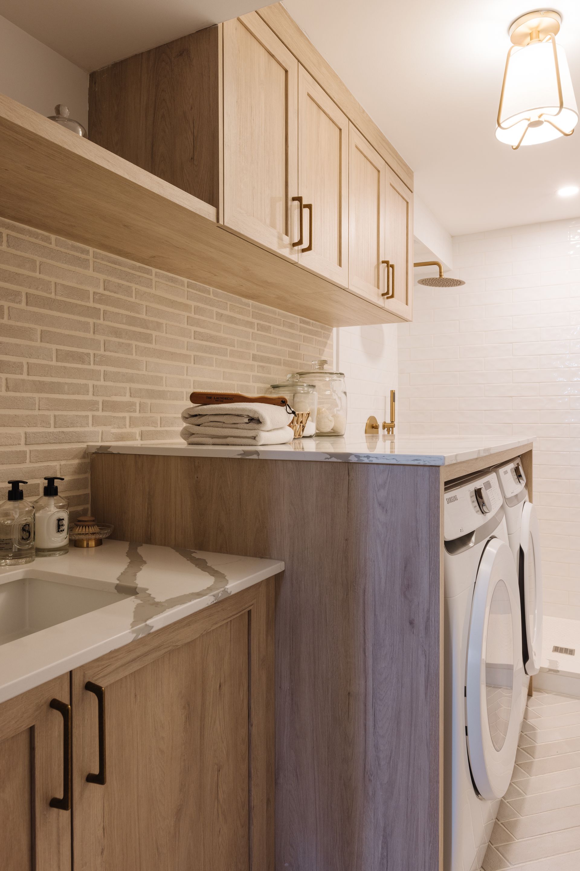 Laundry room with light wood cabinets, white countertops, and white brick backsplash.