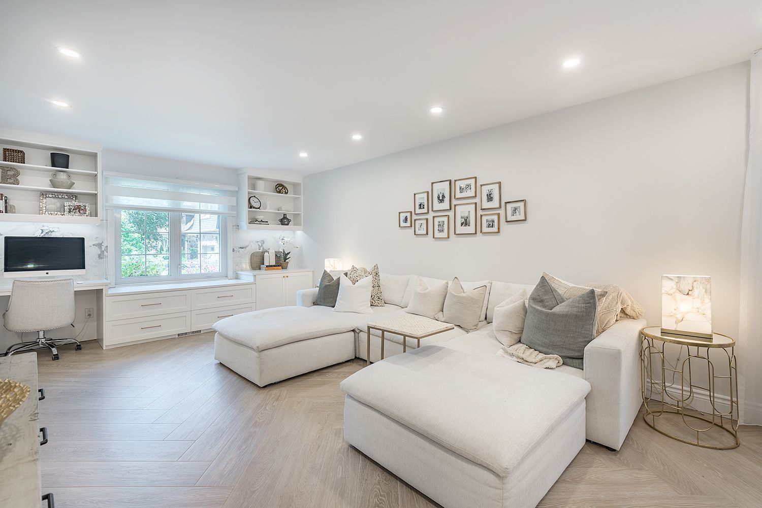 Bright, white living room with a sectional sofa, built-in desk, and art on the wall.