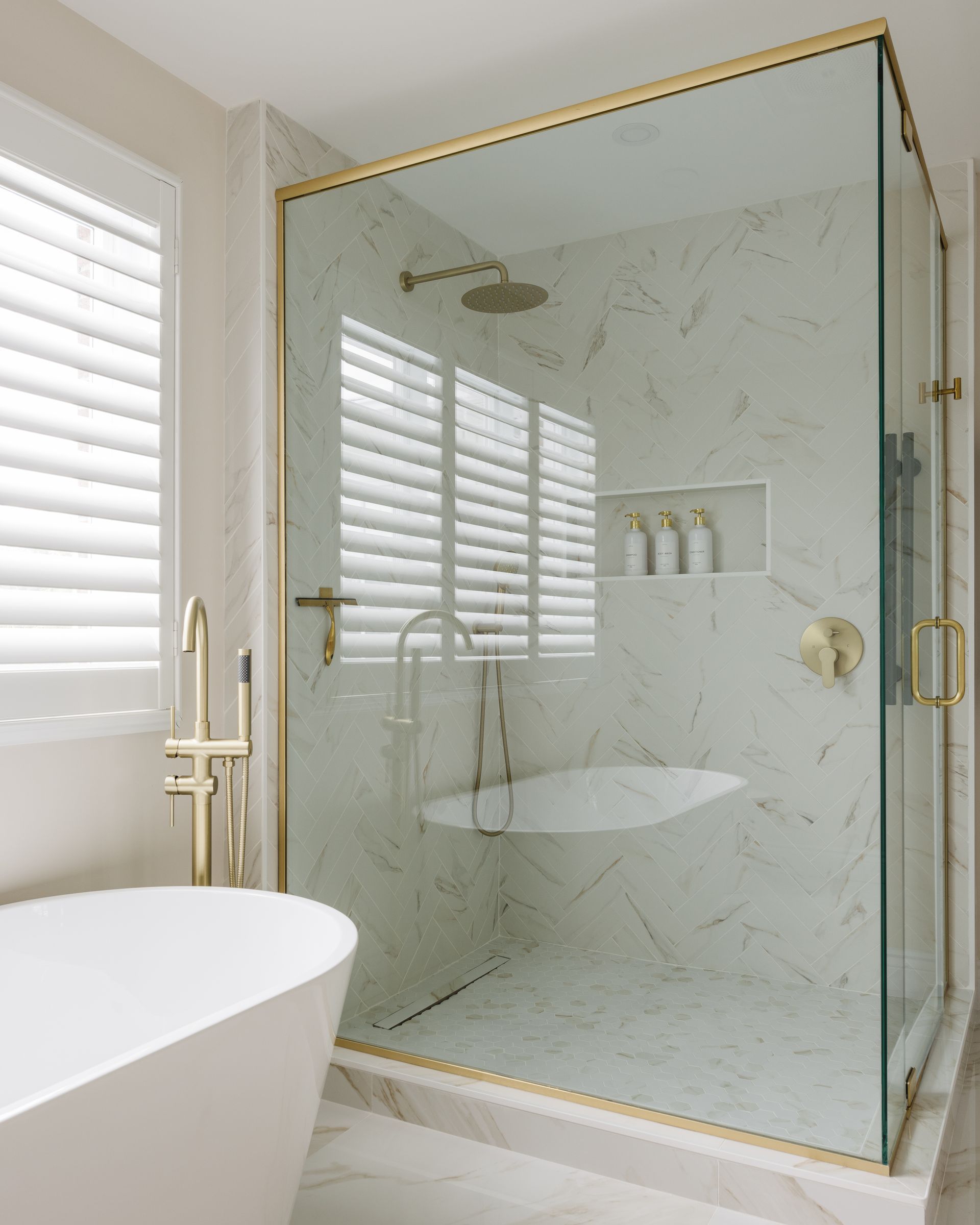 Modern bathroom with gold fixtures, marble shower, glass enclosure, and white tub.