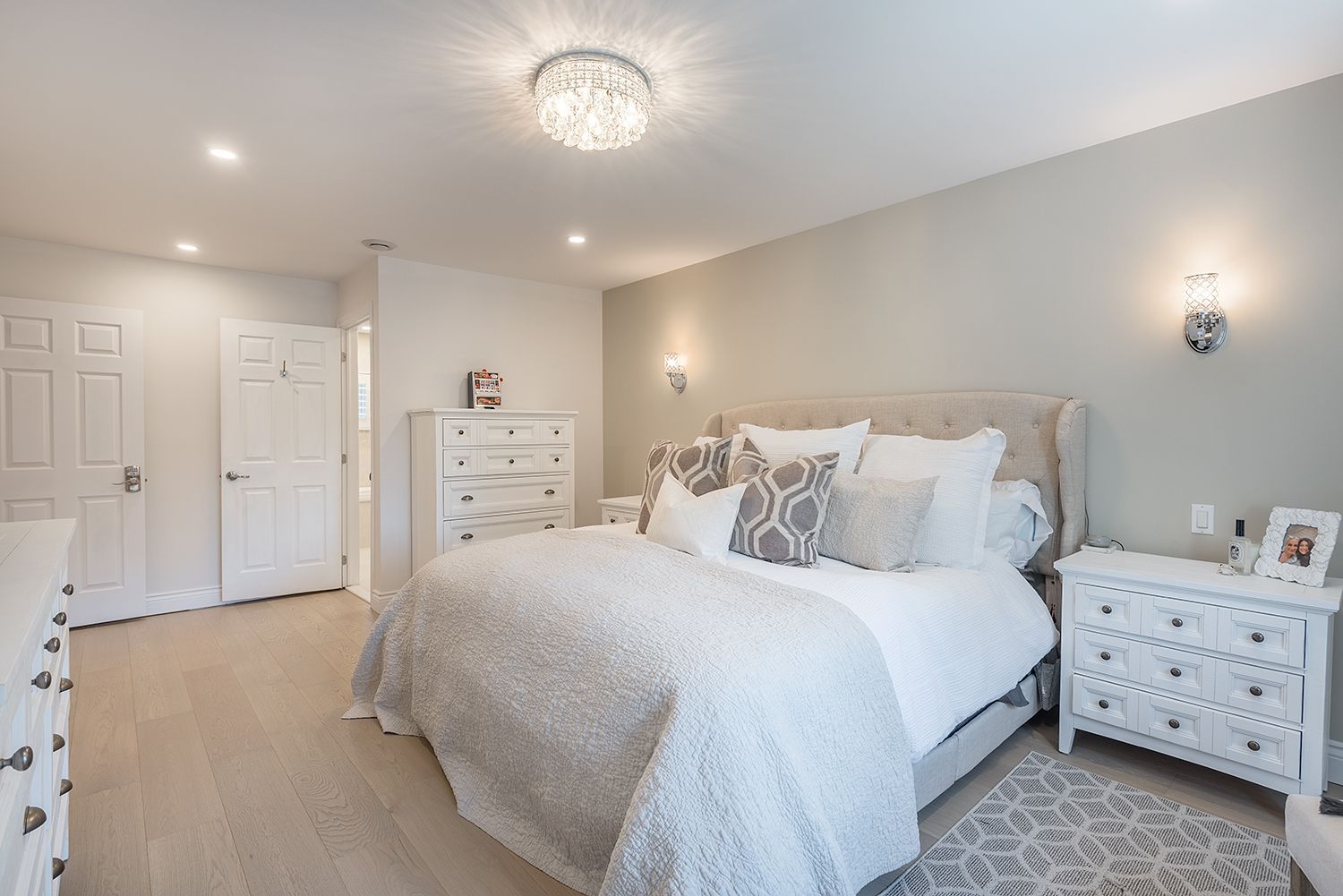 Bedroom with light wood floor, white furniture, gray walls, and bed with white bedding.